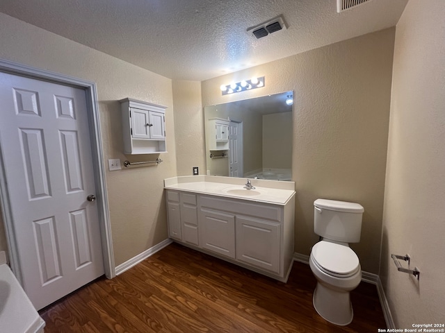 bathroom with a textured ceiling, wood-type flooring, vanity, and toilet