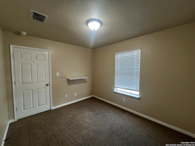 spare room featuring dark carpet and a textured ceiling