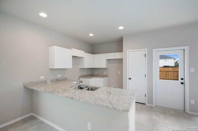 kitchen featuring white cabinets, kitchen peninsula, light stone countertops, light tile patterned floors, and sink