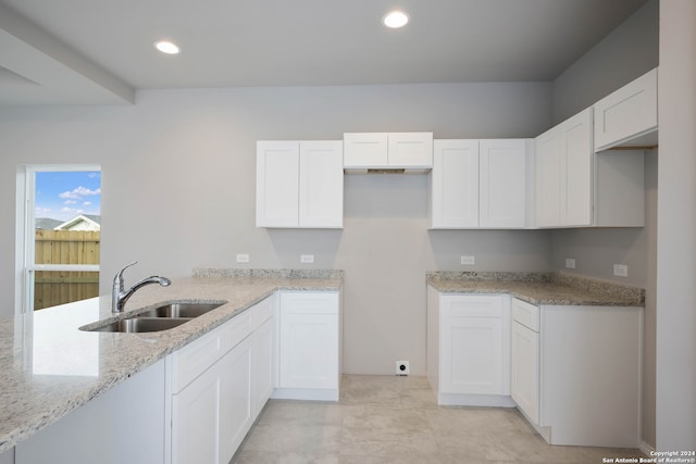 kitchen with light stone countertops, white cabinets, and sink