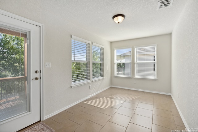 doorway to outside with a textured ceiling, plenty of natural light, and light tile patterned floors