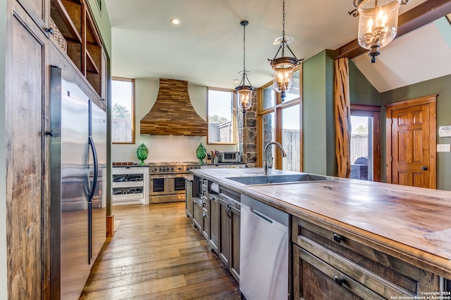 kitchen featuring custom range hood, appliances with stainless steel finishes, light hardwood / wood-style floors, pendant lighting, and sink