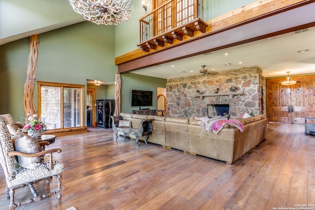 living room with a stone fireplace, a towering ceiling, and hardwood / wood-style floors