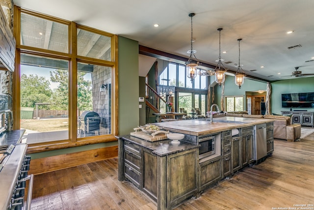 kitchen with ceiling fan, pendant lighting, sink, wood-type flooring, and a kitchen island with sink