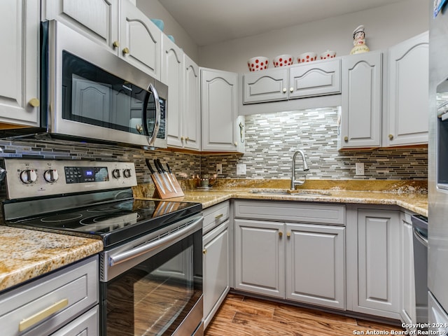 kitchen with light stone counters, sink, light hardwood / wood-style flooring, backsplash, and stainless steel appliances