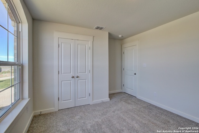 unfurnished bedroom featuring light carpet, a textured ceiling, and a closet