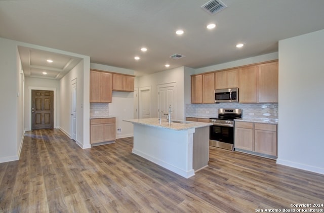 kitchen with light stone counters, stainless steel appliances, hardwood / wood-style flooring, a center island with sink, and sink