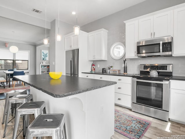 kitchen with appliances with stainless steel finishes, decorative light fixtures, a kitchen breakfast bar, and white cabinets