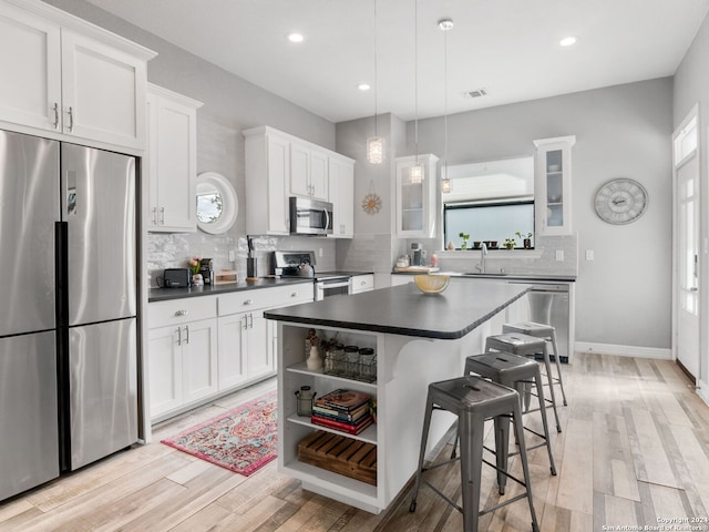 kitchen with pendant lighting, white cabinetry, stainless steel appliances, and light hardwood / wood-style flooring