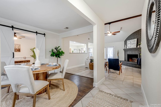 tiled dining room with lofted ceiling, a fireplace, ornamental molding, ceiling fan, and a barn door