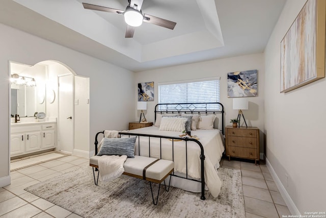 bedroom with light tile patterned floors, ensuite bath, ceiling fan, and a raised ceiling