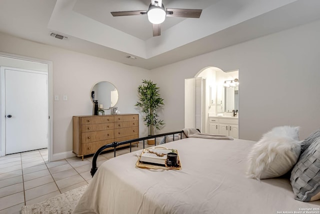 bedroom with ceiling fan, ensuite bathroom, a raised ceiling, and light tile patterned flooring