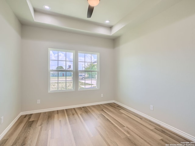 empty room with light hardwood / wood-style floors, ceiling fan, and a tray ceiling