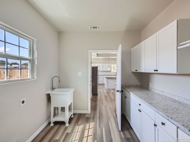 kitchen with light wood-type flooring, stainless steel refrigerator, light stone countertops, and white cabinets