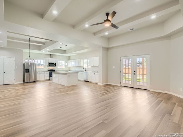 unfurnished living room featuring ceiling fan with notable chandelier, a raised ceiling, light hardwood / wood-style flooring, french doors, and sink