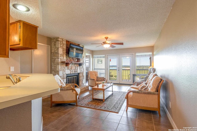 tiled living room with a stone fireplace, ceiling fan, sink, and a textured ceiling