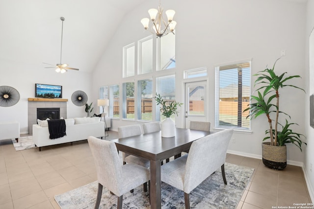 dining space with ceiling fan with notable chandelier, light tile patterned floors, high vaulted ceiling, and a fireplace