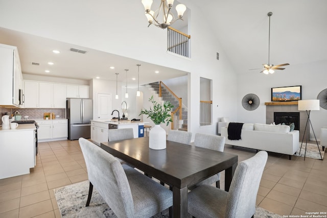 dining space featuring ceiling fan with notable chandelier, a fireplace, light tile patterned floors, and high vaulted ceiling