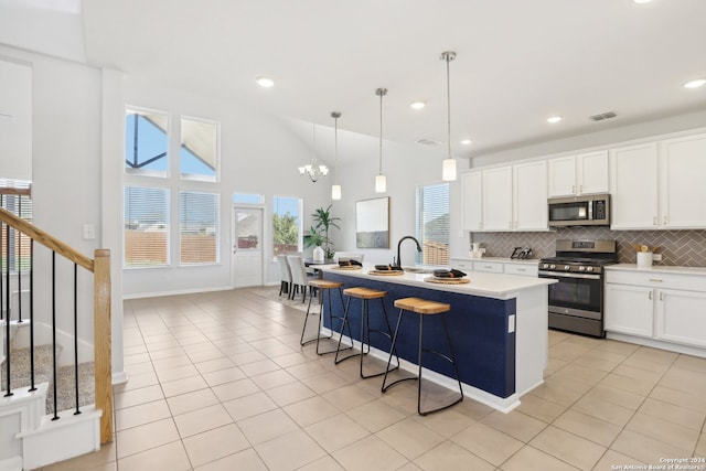 kitchen with white cabinetry, an island with sink, pendant lighting, stainless steel appliances, and an inviting chandelier