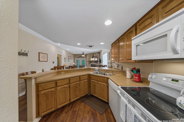 kitchen with hanging light fixtures, sink, kitchen peninsula, white appliances, and dark hardwood / wood-style floors