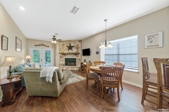 dining area featuring dark hardwood / wood-style flooring, ceiling fan with notable chandelier, plenty of natural light, and a stone fireplace