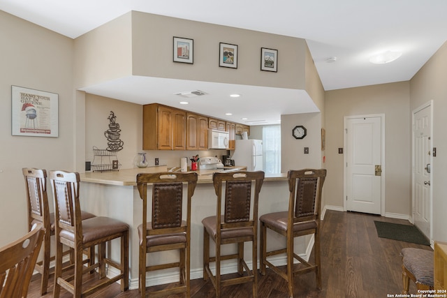 kitchen with kitchen peninsula, dark hardwood / wood-style floors, a kitchen bar, and white appliances