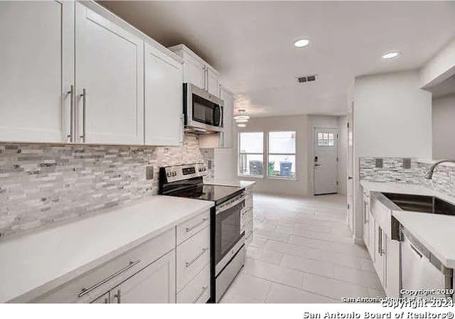 kitchen with backsplash, white cabinetry, sink, and stainless steel appliances