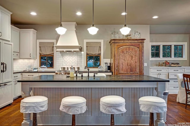 kitchen with a breakfast bar, decorative light fixtures, dark hardwood / wood-style floors, and a kitchen island with sink