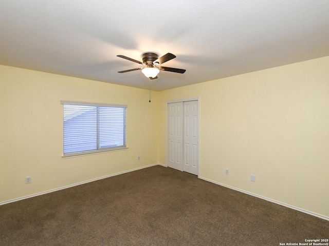 unfurnished bedroom featuring dark colored carpet, a closet, and ceiling fan