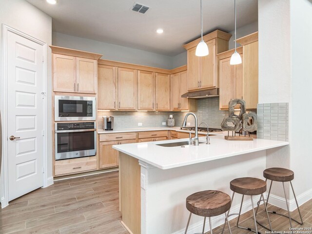 kitchen featuring a sink, a peninsula, light brown cabinetry, and stainless steel appliances