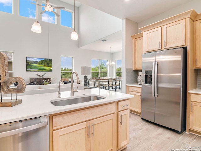 kitchen featuring light countertops, light brown cabinetry, under cabinet range hood, a sink, and light wood finished floors