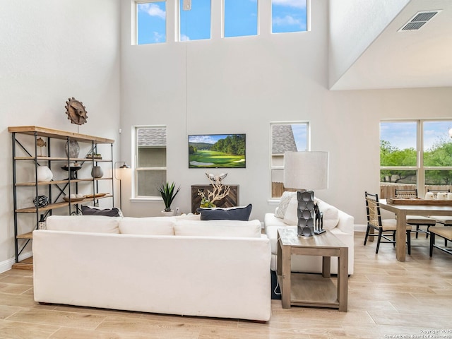 living room with baseboards, a high ceiling, a ceiling fan, and light wood finished floors