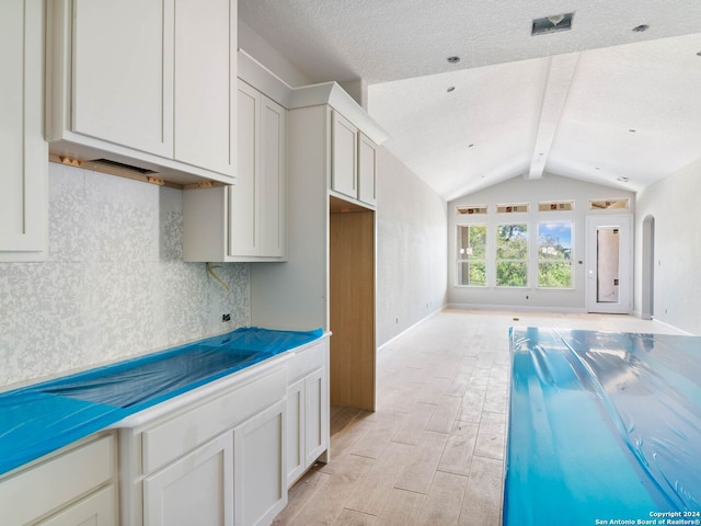 kitchen with lofted ceiling with beams, white cabinetry, backsplash, light wood-type flooring, and a textured ceiling