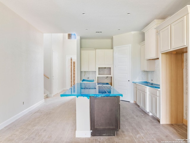 kitchen featuring light hardwood / wood-style floors, a textured ceiling, tasteful backsplash, white cabinetry, and a kitchen island