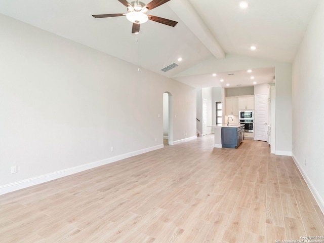 unfurnished room featuring light wood-style floors, lofted ceiling with beams, a textured ceiling, baseboards, and arched walkways