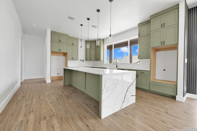 kitchen with light hardwood / wood-style floors, a center island, green cabinetry, hanging light fixtures, and light stone countertops