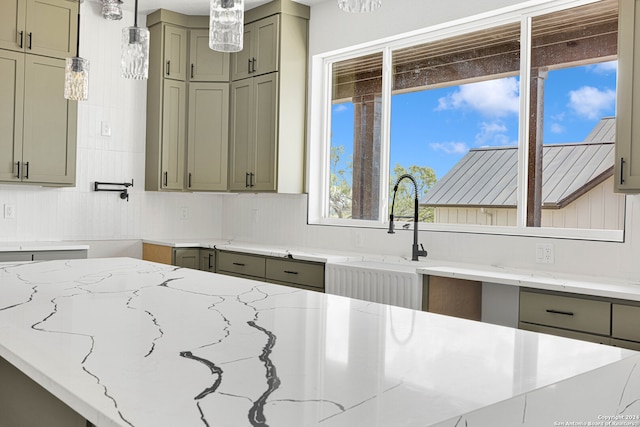 kitchen featuring sink, green cabinets, light stone counters, and decorative light fixtures