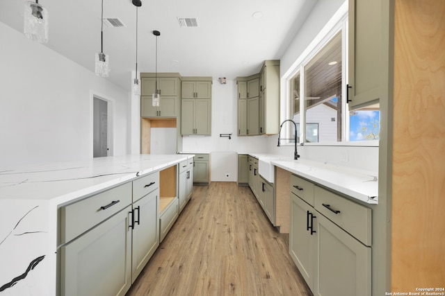 kitchen with decorative light fixtures, light hardwood / wood-style flooring, sink, and light stone countertops