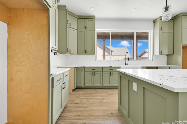 kitchen with light wood-type flooring, green cabinetry, light stone countertops, and pendant lighting