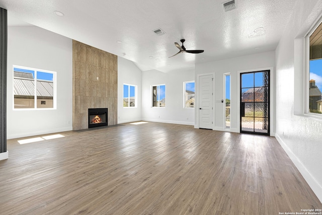 unfurnished living room with ceiling fan, wood-type flooring, a textured ceiling, a tiled fireplace, and vaulted ceiling