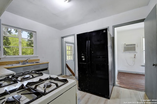 kitchen with sink, white range with gas stovetop, light wood-type flooring, black refrigerator, and an AC wall unit