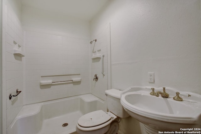 bathroom with tiled shower, toilet, and sink