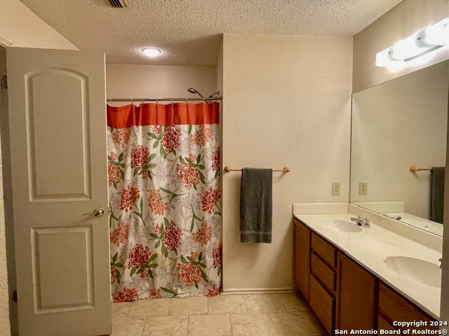 bathroom featuring a shower with curtain, a sink, a textured ceiling, and double vanity