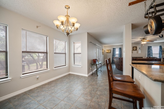 tiled dining area with a sink, ceiling fan with notable chandelier, baseboards, and a textured ceiling