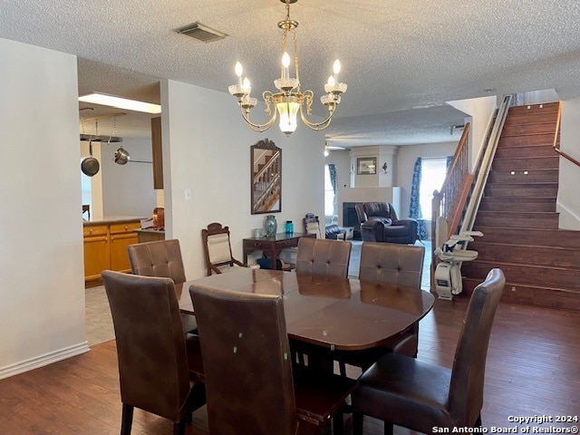 dining space with a textured ceiling, a notable chandelier, wood finished floors, visible vents, and stairway