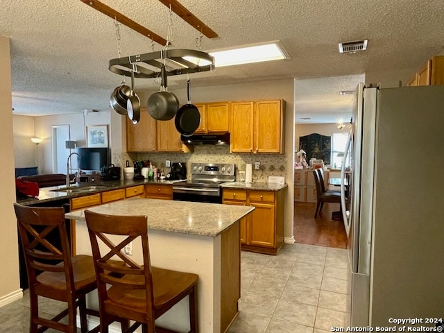 kitchen featuring visible vents, appliances with stainless steel finishes, a sink, under cabinet range hood, and a kitchen breakfast bar