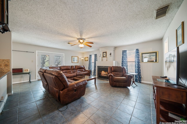living room with visible vents, dark tile patterned floors, a ceiling fan, and a fireplace with flush hearth