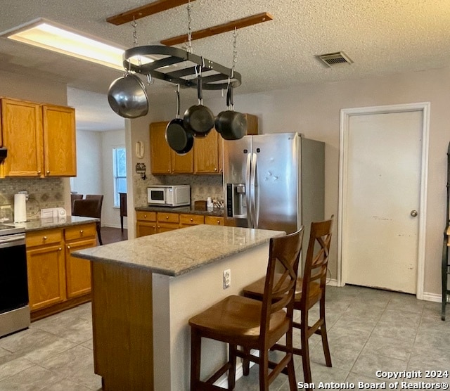 kitchen with tasteful backsplash, visible vents, appliances with stainless steel finishes, and brown cabinetry