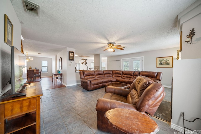 tiled living area featuring a textured ceiling, ceiling fan with notable chandelier, visible vents, and a wealth of natural light