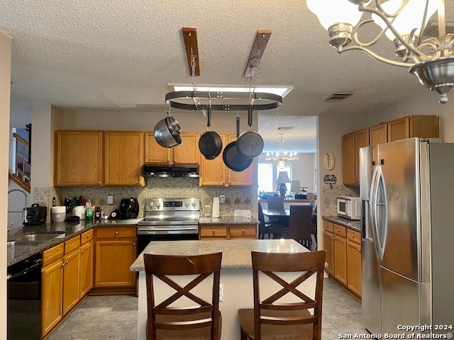 kitchen with decorative backsplash, appliances with stainless steel finishes, a sink, a chandelier, and under cabinet range hood